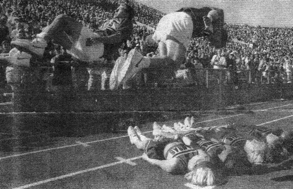 Newspaper photo of little Greg and me front-flipping over some people while cheerleading at a KU football game.